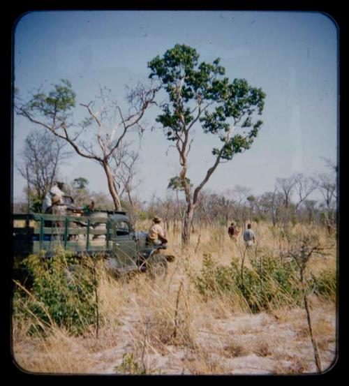 Expedition members gathering in a truck, with Ju/'hoan men walking ahead of them