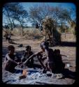 Family: !U and her children sitting by fire, with skerms in the background