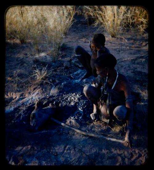 Food, Cooking: Elderly woman poking animal head in ashes, with a boy beside her