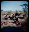 Food, Meat: Man squatting and cutting up meat, with a group of people, including ≠Toma, in the background