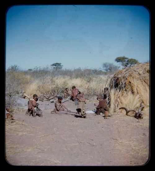 Food, Meat: Group of people sitting in front of a skerm, with a man with meat in the background and horns lying against skerm in the foreground