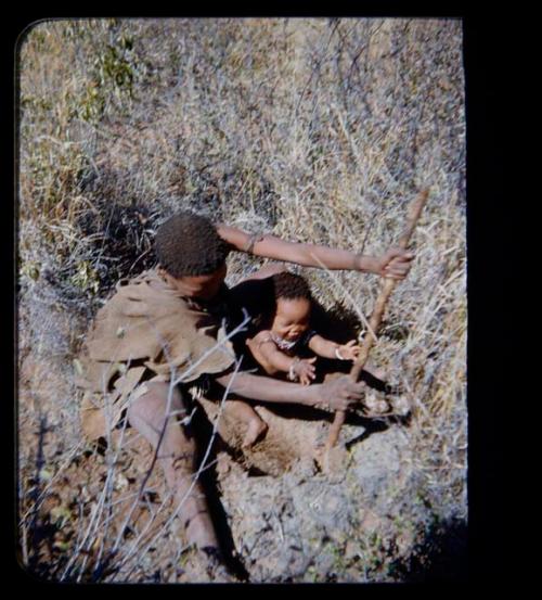 Food Gathering, Children: Woman sitting in grass digging, with a child reaching for a stick