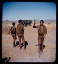 Greeting gesture: Man demonstrating a greeting gesture, with two other men and a  truck in the background