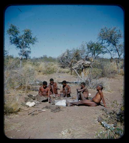 Groups, Men: Group of men sitting, including one working on animal hide and another with mortar and pestle