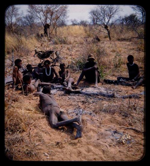 Groups, Men: Group of people sitting by ashes of fire, with one wearing western clothes