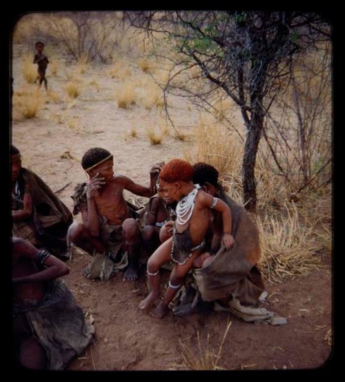 Hair Cutting: Group of women and children, including one child with red powder in hair