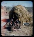 Groups: Group of women and children sitting by a skerm, with two ostrich eggs on the ground nearby