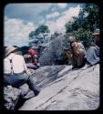 John Marshall using a Polaroid camera, sitting with Elizabeth Marshall Thomas, Lorna Marshall and Laurence Marshall on rocks above the Okavango River