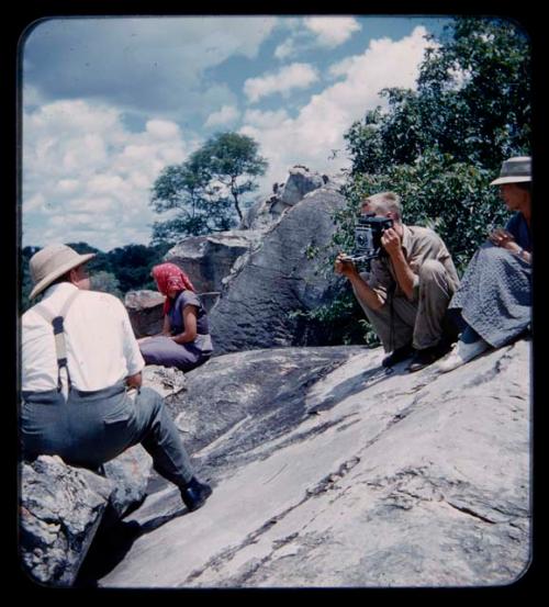 John Marshall using a Polaroid camera, sitting with Elizabeth Marshall Thomas, Lorna Marshall and Laurence Marshall on rocks above the Kavango River