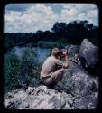 John Marshall using a Polaroid camera, sitting on rocks above the Kavango River