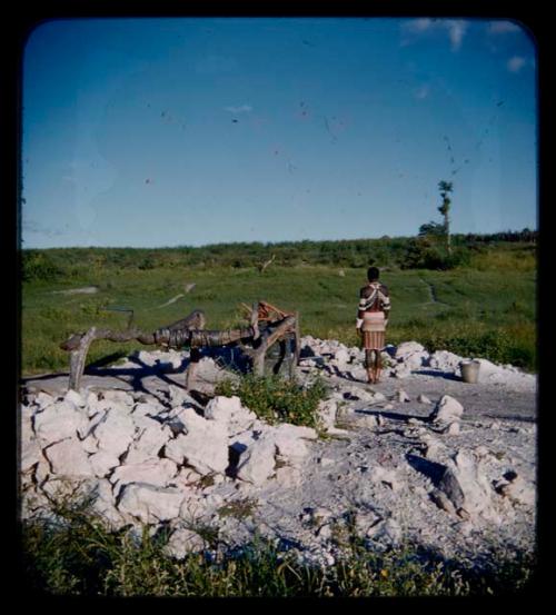 Makiena (wife of Muremi) standing next to a waterhole, looking at a kraal, view from behind