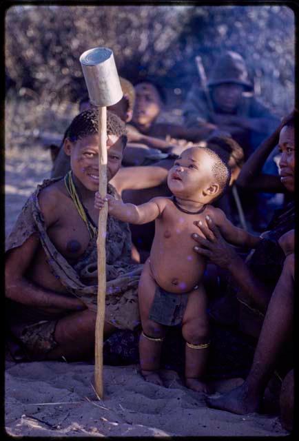 Group of people sitting, child standing holding a stick