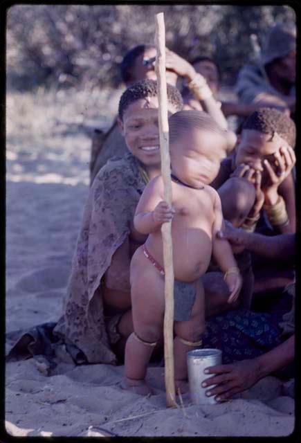 Group of people sitting, child standing holding a stick