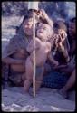 Group of people sitting, child standing holding a stick