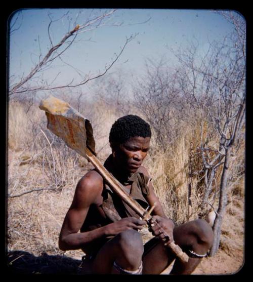 Music: Man squatting and holding a one-stringed violin over his shoulder