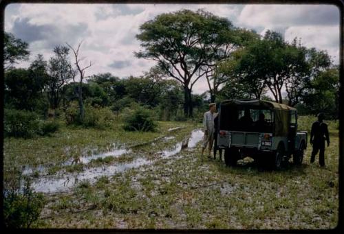 John Marshall and Louis standing near Land Rover on wet road through trees