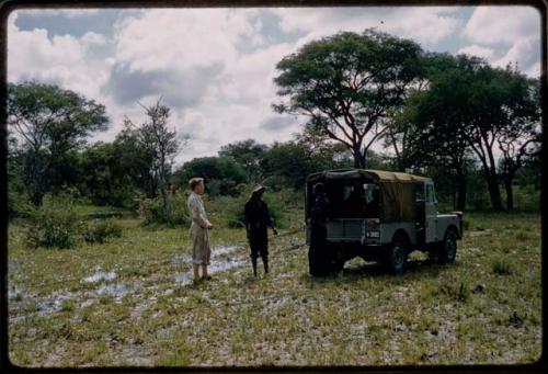 John Marshall, Louis, and Kernel Ledimo standing near Land Rover on wet road through trees