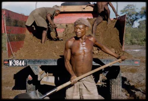 Man spreading fertilizer behind a truck, with other people working on the truck in the background