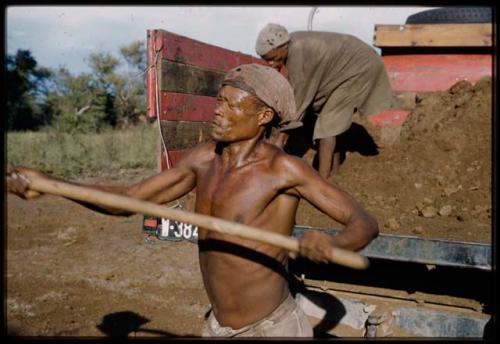 /Ti!kay and another man shoveling fertilizer from the back of the expedition truck