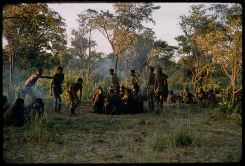 Men performing a curing dance, with a group of people sitting and watching them