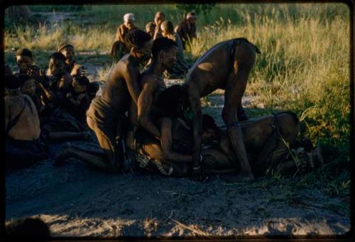 Medicine man falling in trance, held by the others, with a group of people watching them in the background