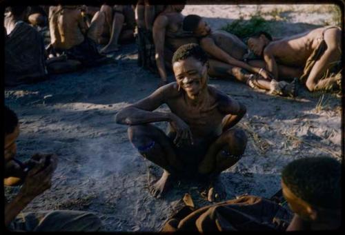 Man squatting, with a row of men in trance in the background