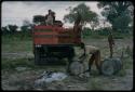 Louis loading barrels on a red truck, with other men watching him