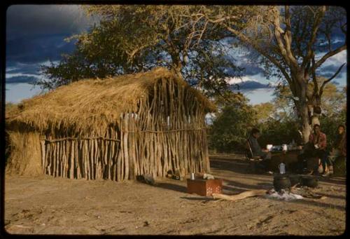 Exterior of a cookhouse, with people sitting at a table nearby