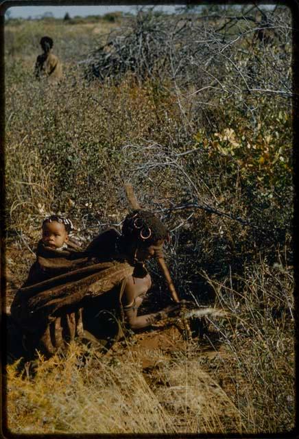 Woman digging the ground with a stick, with a child on her back