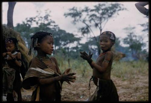 Two girls clapping at !’hu kuitzi (veldkos game), with another girl in the background