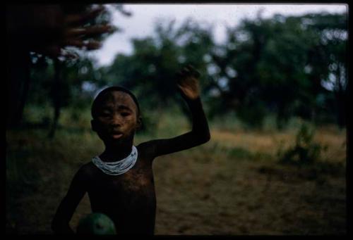 Child holding a veldkos in one hand and raising the other, !’hu kuitzi (veldkos game)