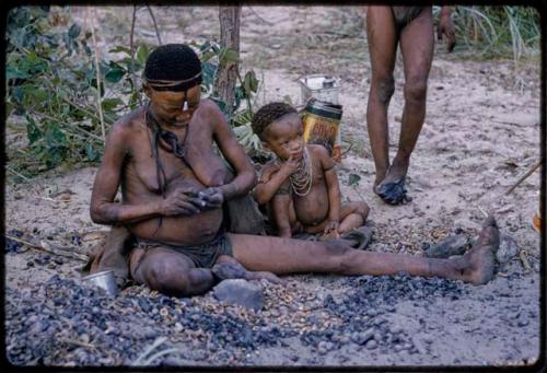 !U shelling mangetti nuts, sitting with one of her children