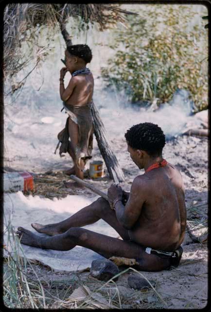 ≠Toma in profile sitting in the shade, with Norna standing nearby