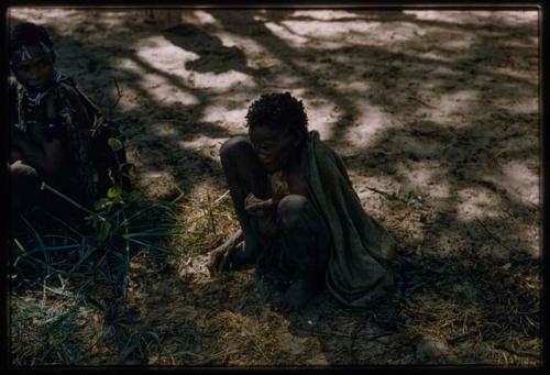 Elderly woman sitting on the ground, with another woman sitting beside her