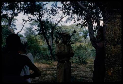 Four men standing near a tree, including two men wearing Western clothes