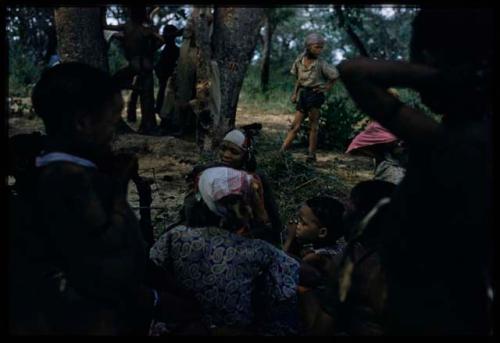 Group of people gathered near a tree, including some people wearing Western clothes