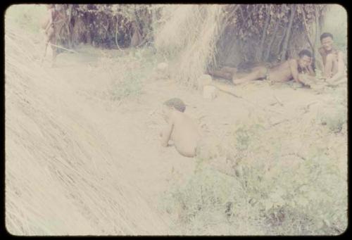 Man lying on the ground, with a group of people under a skerm in the background