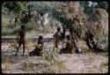 Group of women and children sitting on the ground, with skerms nearby