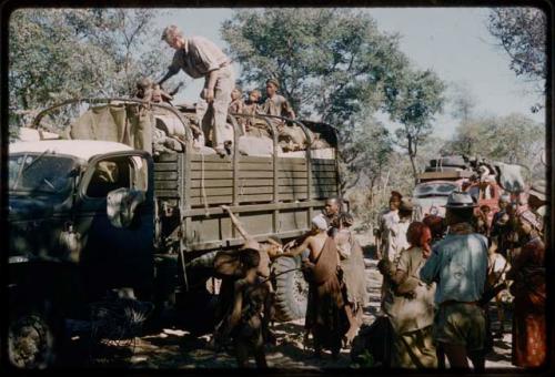 Group of people and John Marshall riding on a green expedition truck to get water, with other people standing around it