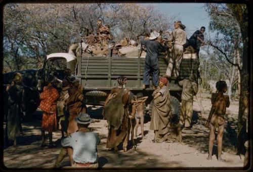 Group of people and John Marshall riding on a green expedition truck to get water, with other people standing nearby