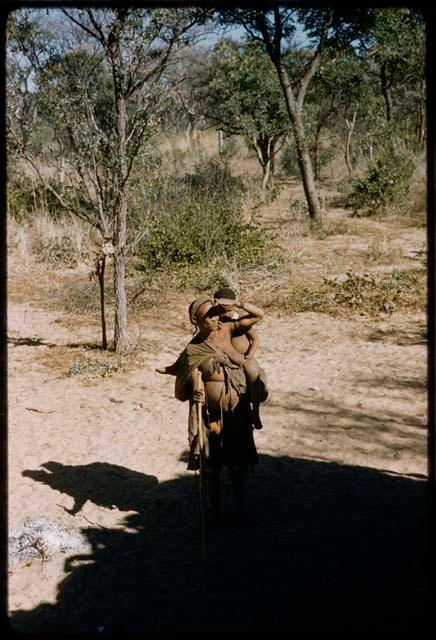 Woman, with a baby on her back, shading her eyes to watch something