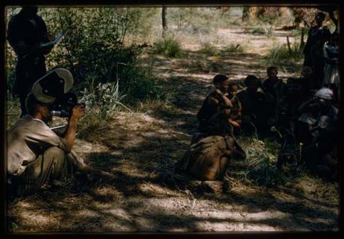 John Marshall squatting and filming a group of people