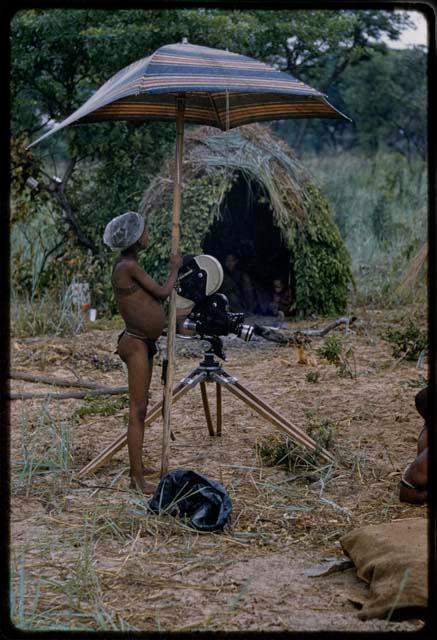 Boy standing and holding a camera under an umbrella  with a skerm in the background