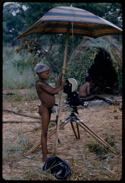 Boy standing and holding a camera under an umbrella  with a skerm in the background