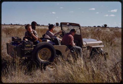 John Marshall driving a truck and Elizabeth Marshall Thomas eating something in the backseat, with two other people present