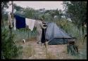 Charles Koch closing a tent, with clothes hanging on a line behind him