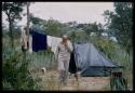 Charles Koch walking away from a tent, with clothes hanging on a line behind him