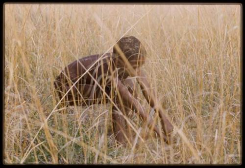 Boy squatting and looking for something in long grass