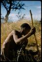 Man squatting in the grass with a digging stick