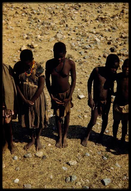 Group of people standing, including a girl wearing a red dress, view from the expedition truck